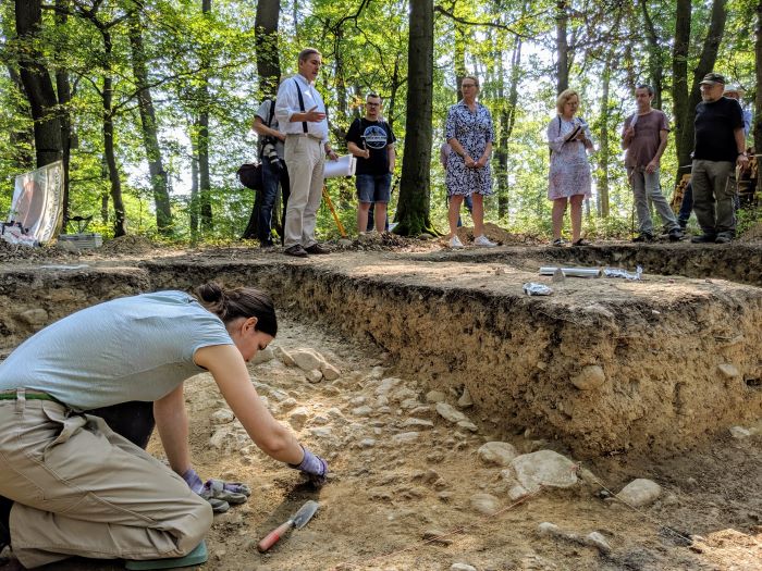 Bei Grabungen am Kapellenberg bei Hofheim am Taunus entdeckten Archäologen vermutlich ein jungsteinzeitliches Grubenhaus. In der Mitte des Bildes sieht man den Eingangsbereich. Menschen im Hintergrund einer Grabung, vorn untersucht eine Mitarbeiterin den Grabungsort