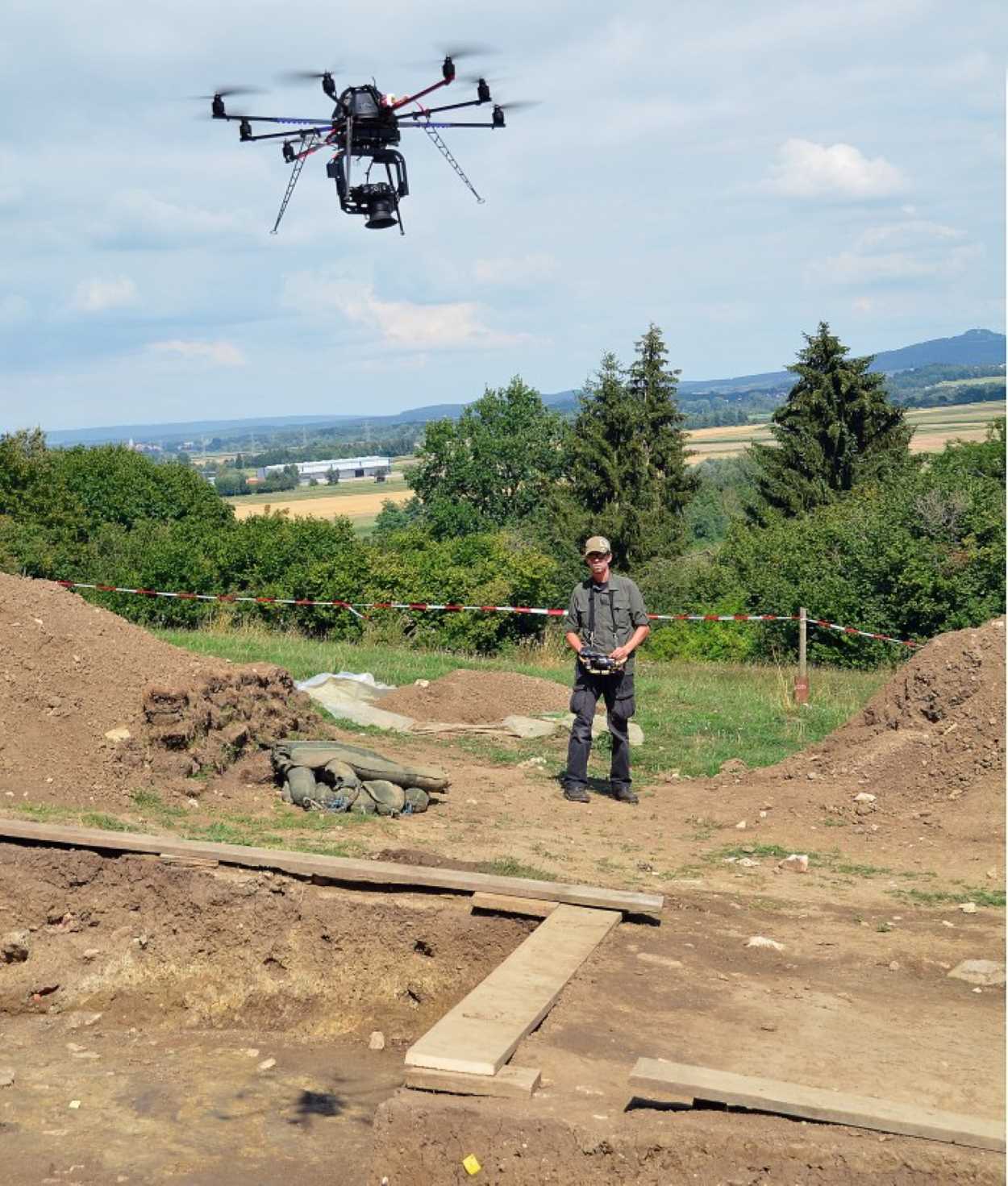 Dokumentation einer Grabung mit Drohnen-Einsatz. Mitarbeitender steuert eine Drohne über einer Ausgrabung.